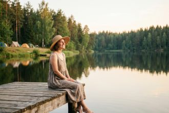 Femme assise sur un ponton en bois au bord d'un lac paisible entouré de forêt, lors d'un séjour en camping d'été