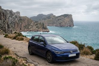 Voiture compacte garée sur une route côtière étroite d'une île avec falaises et mer turquoise en arrière-plan